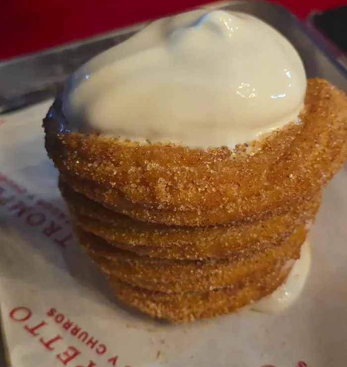 Una torre de churro con azúcar y canela, coronada de crema, sobre el papel rojo y blanco de Trompetto